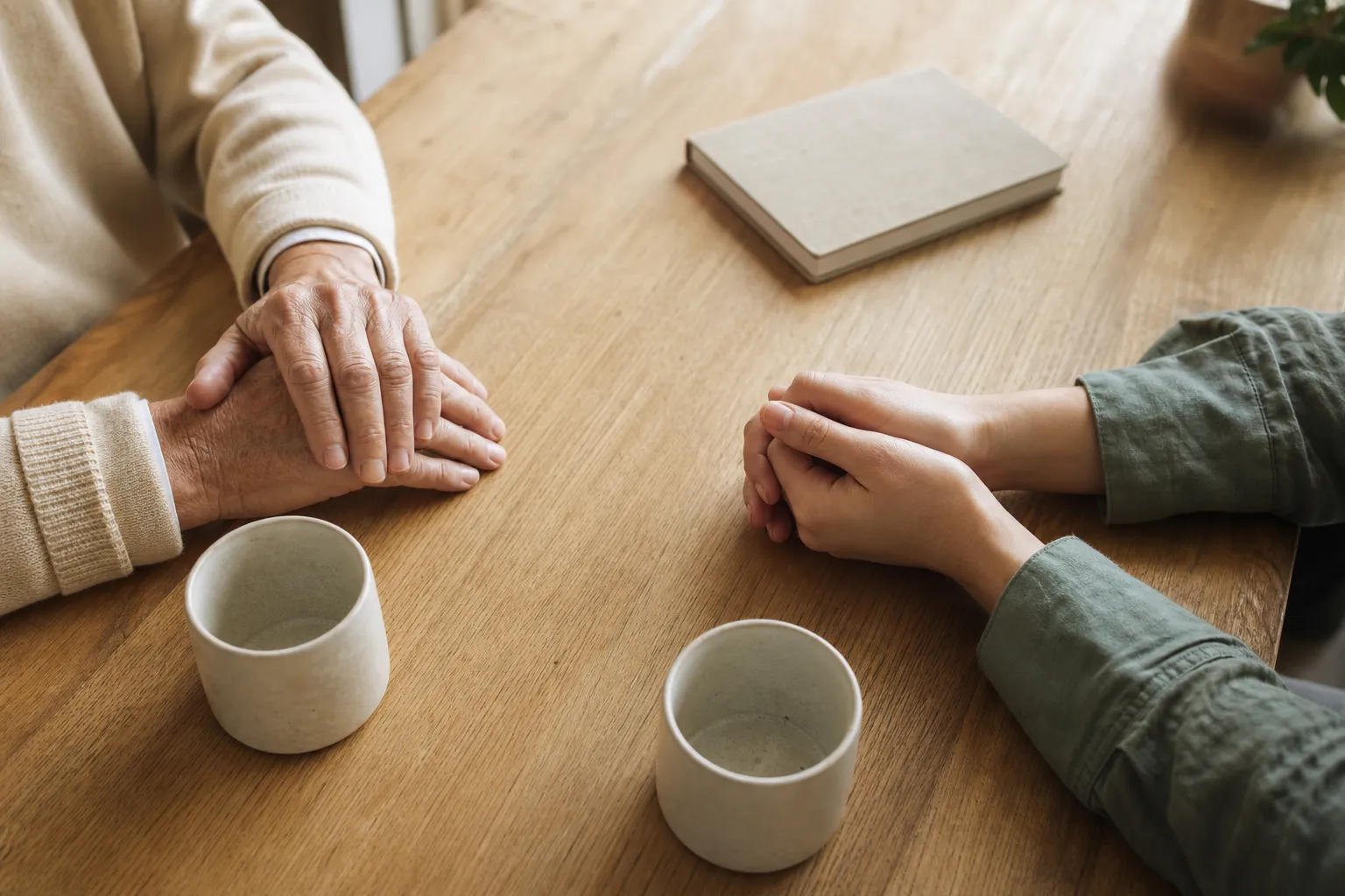 Deux paires de mains posées sur une table, conversation calme, tasses vides à côté